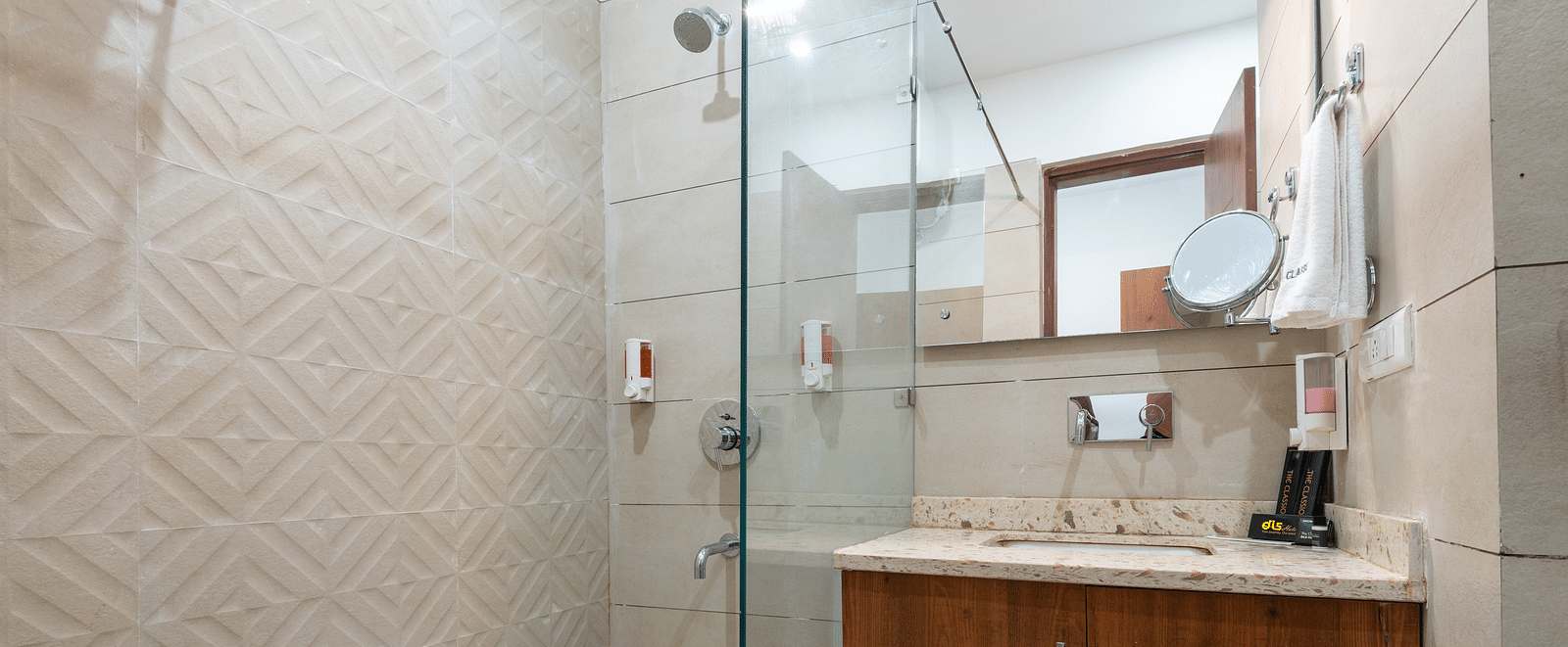Deluxe bathroom featuring a mirror above a washbasin with a wooden cabinet below and a spacious shower area at DLS The Classio